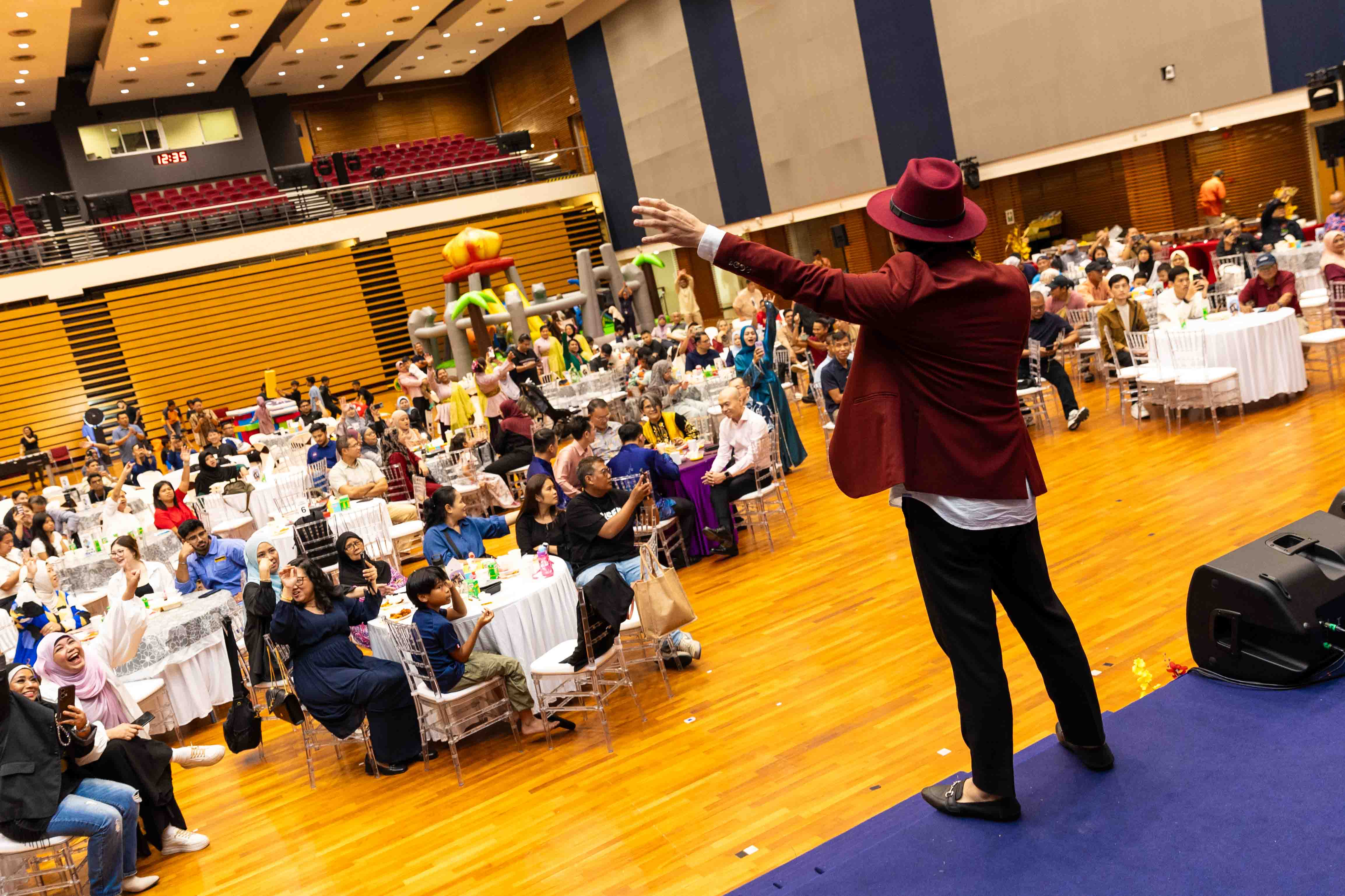 Members seated at round tables watch and respond to a stage performance.